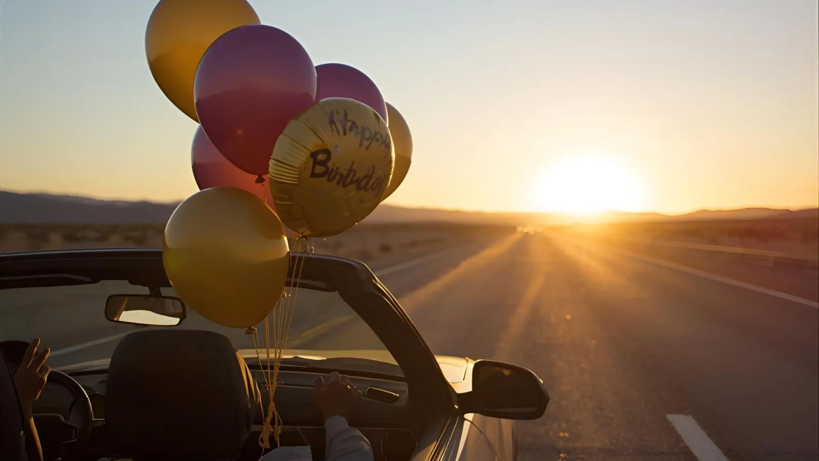 Car driving down a highway at sunset with birthday balloons inside during a birthday road trip.